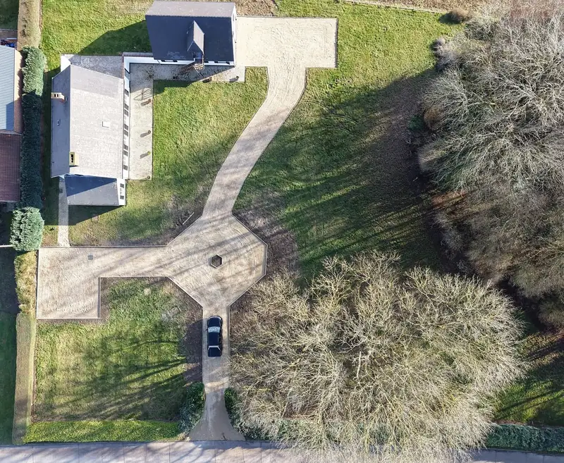 Vue aérienne après travaux : allée en gravier clair bordée, avec rond-point paysager et zone de stationnement