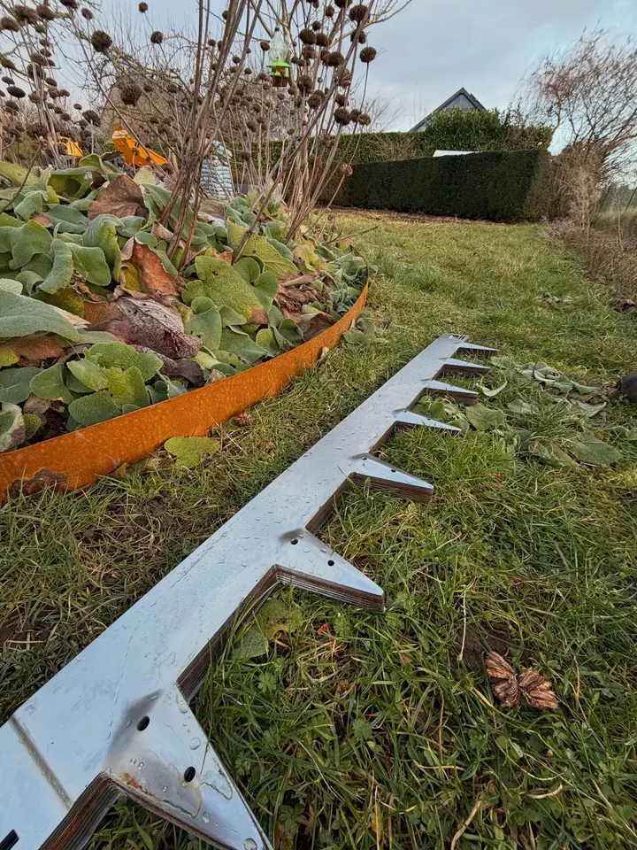 Bordure en acier corten le long d'un massif, élément de bordure prêt à poser au premier plan