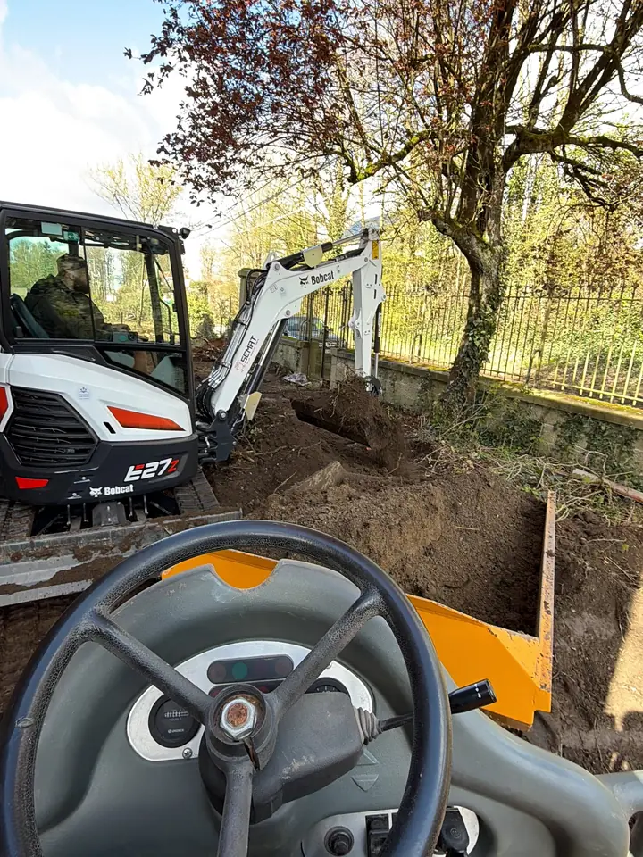 Le dumper vu depuis le poste de conduite, à côté d'une mini-pelle qui creuse