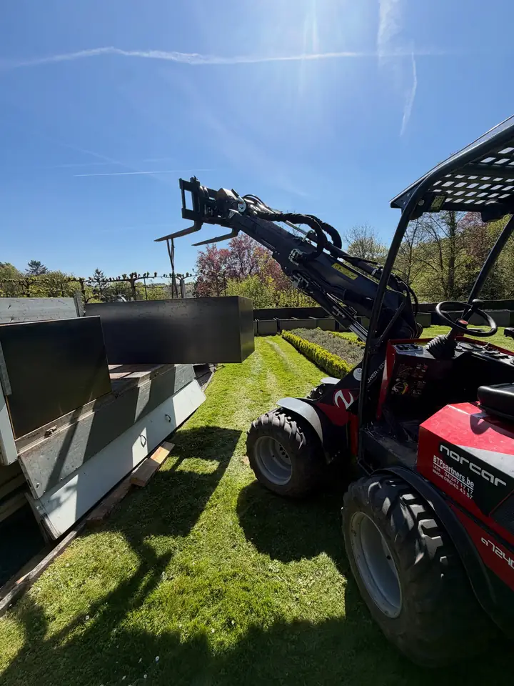 Chargeuse Norcar équipée de fourches à palette, au bord d'une pelouse